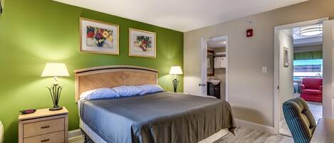 A bedroom with a bed, nightstands, a chair, and a door leading to a bathroom.