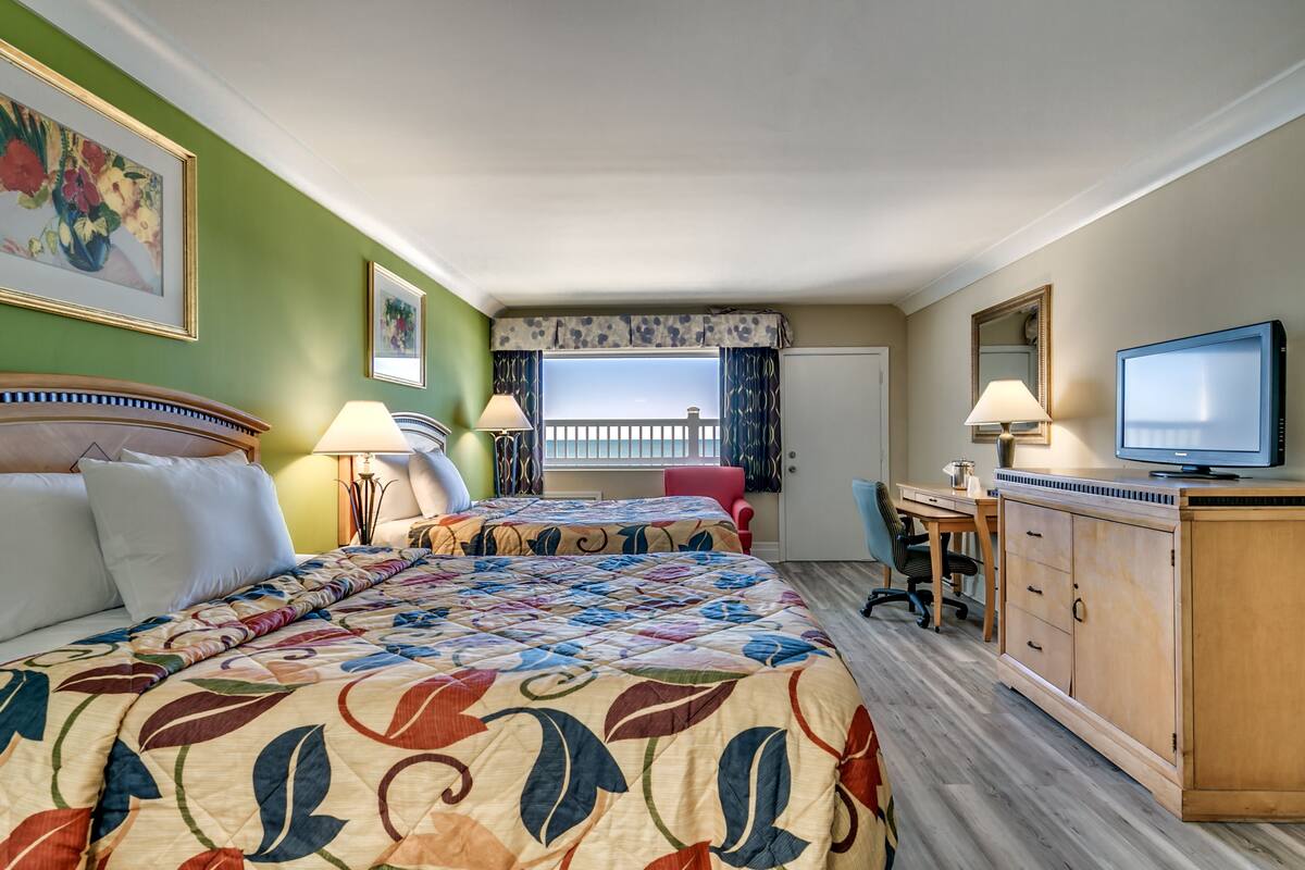 Une chambre d’hôtel avec deux lits, un bureau, une télévision et un balcon avec vue.