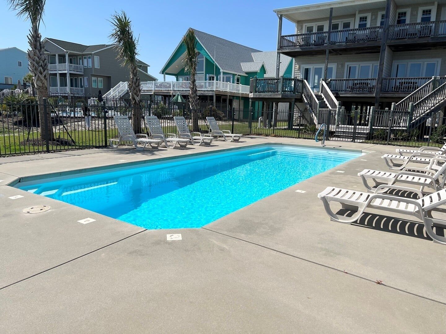 A swimming pool with lounge chairs and a multi-story building with balconies in the background.