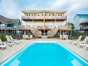 Un hotel con piscina, mobiliario exterior y un edificio de varios pisos con balcones.