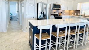 A modern kitchen with white cabinets, stainless steel appliances, a central island with bar stools, and a ceiling fan.