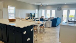 A modern kitchen with a central island, dining area with chairs, a sofa, and a TV.