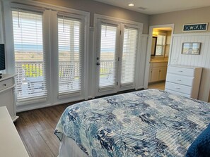 Un dormitorio con cama, cómoda, televisor y vista al océano a través de una puerta corrediza.
