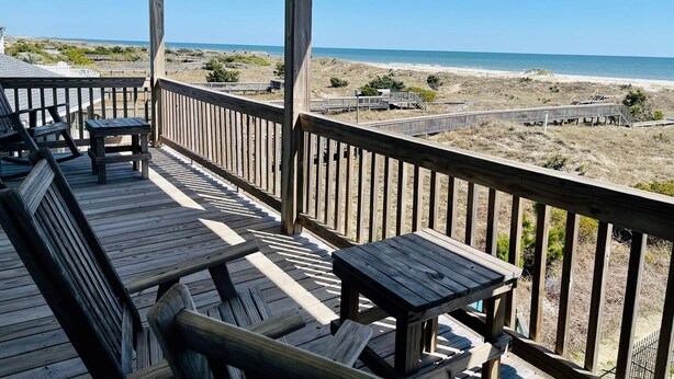 A wooden deck with outdoor seating, overlooking a beach and ocean.