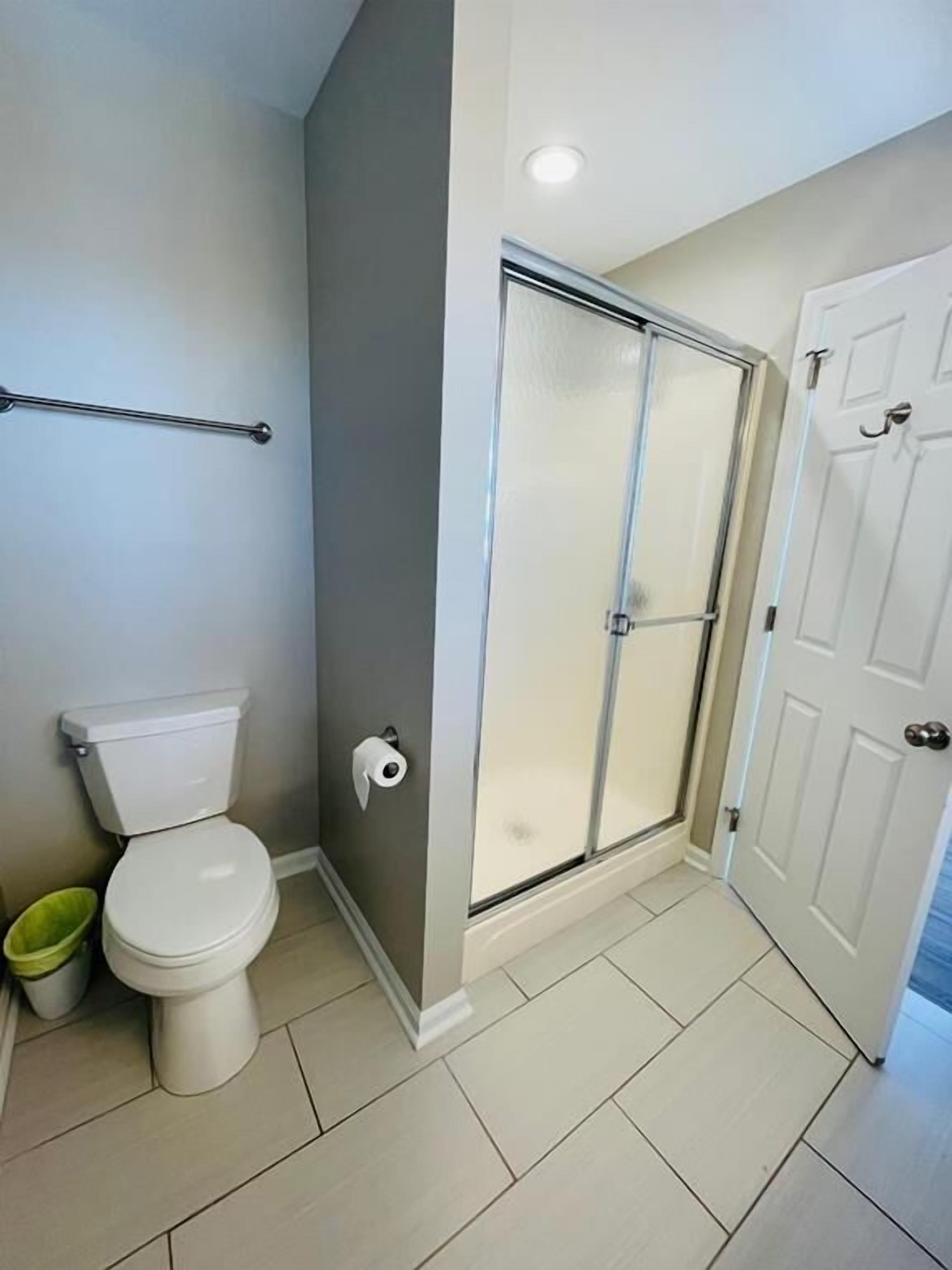 A bathroom with a toilet, a glass-enclosed shower, and a white door.