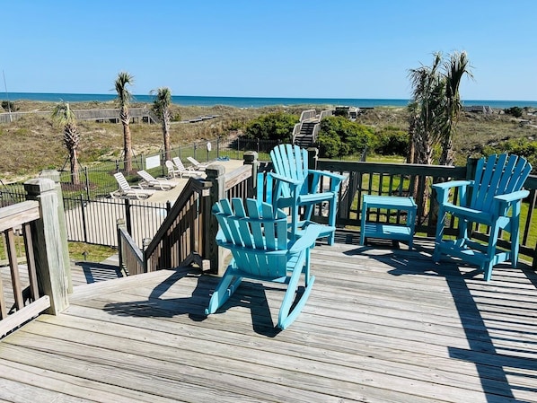 Une terrasse en bois avec des fauteuils Adirondack turquoise et une vue sur lâocĂ©an.