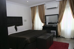 A bedroom with a bed, a desk, a chair, a mirror, and a red rug. - Angel Hospitality Services (Lagos)