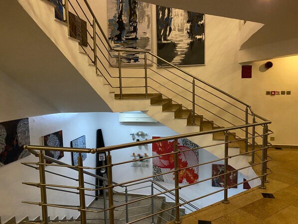 A staircase with metal railings leading to a lower level, surrounded by various artworks on the walls.