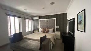 A modern bedroom with a large bed, a sofa, a bedside table, and a TV. - Angel Hospitality Services (Lagos)