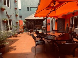 An outdoor patio with a round table and chairs, surrounded by potted plants and a thatched-roof structure. - Angel Hospitality Services (Lagos)