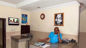 Un comptoir d’accueil avec une personne assise derrière, une horloge et un tableau encadré accroché au mur.
