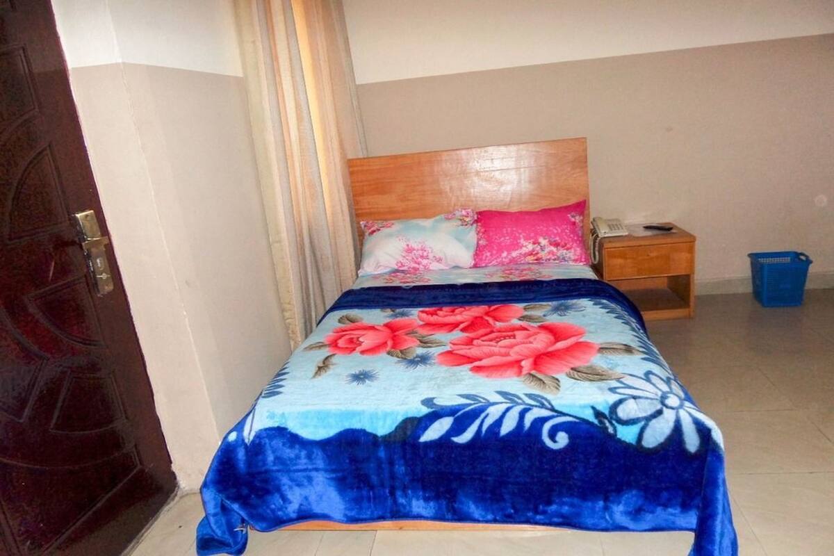 A bedroom with a bed, a wooden headboard, a nightstand, a telephone, and a blue trash bin.