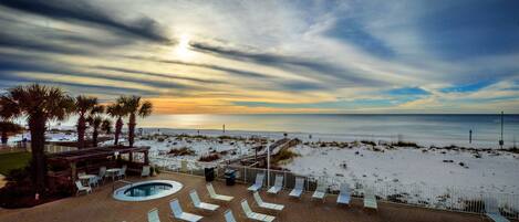 Zona de piscina con sillones de descanso, bañera de hidromasaje y vista a la playa y al océano al atardecer.