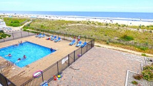 A pool area with a view of the beach, surrounded by a fence and lounge chairs. - Towers 201 2 Bedroom Condo by RedAwning (Ocean City)