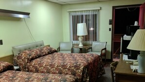 A hotel room with two beds, a desk, a chair, a lamp, and a window with blinds. - Allen's Budget Motel (Watertown)