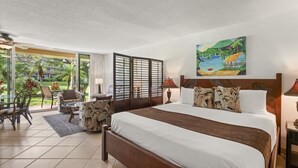 A hotel room with a large bed, a seating area with chairs, a glass door leading to a garden, and a painting on the wall. - Maui Kaanapali S #b133 Studio Bedroom Condo by RedAwning (Lahaina)
