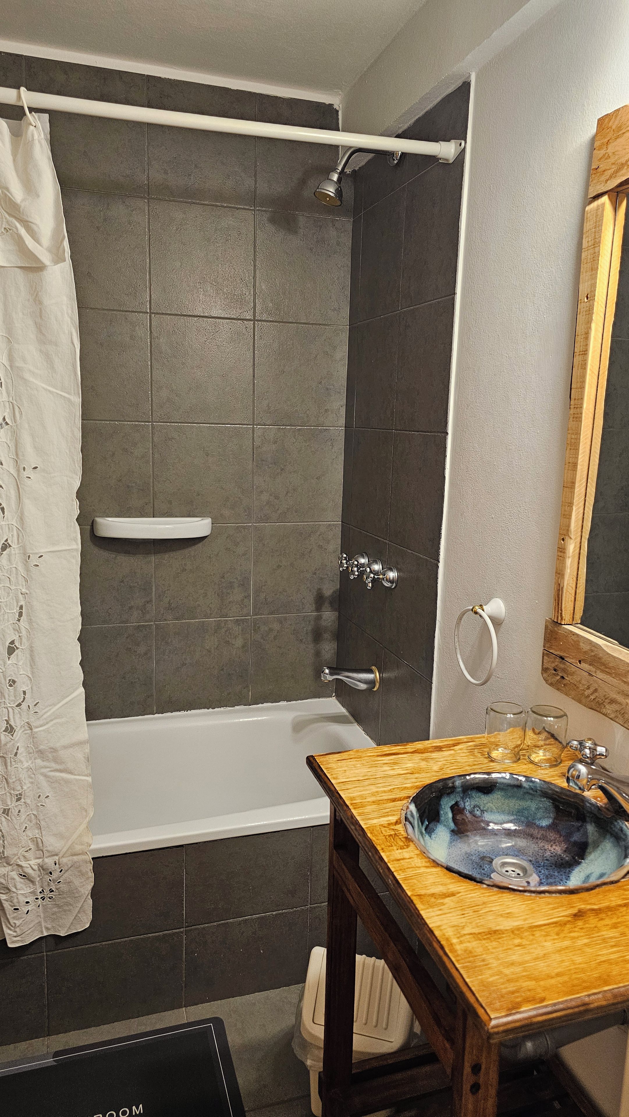 A bathroom with a bathtub, a shower, a sink with a glass basin, and a wooden vanity.