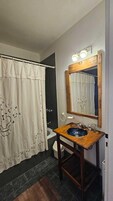 Un baño con tocador de madera, lavamanos, espejo y cortina de ducha.