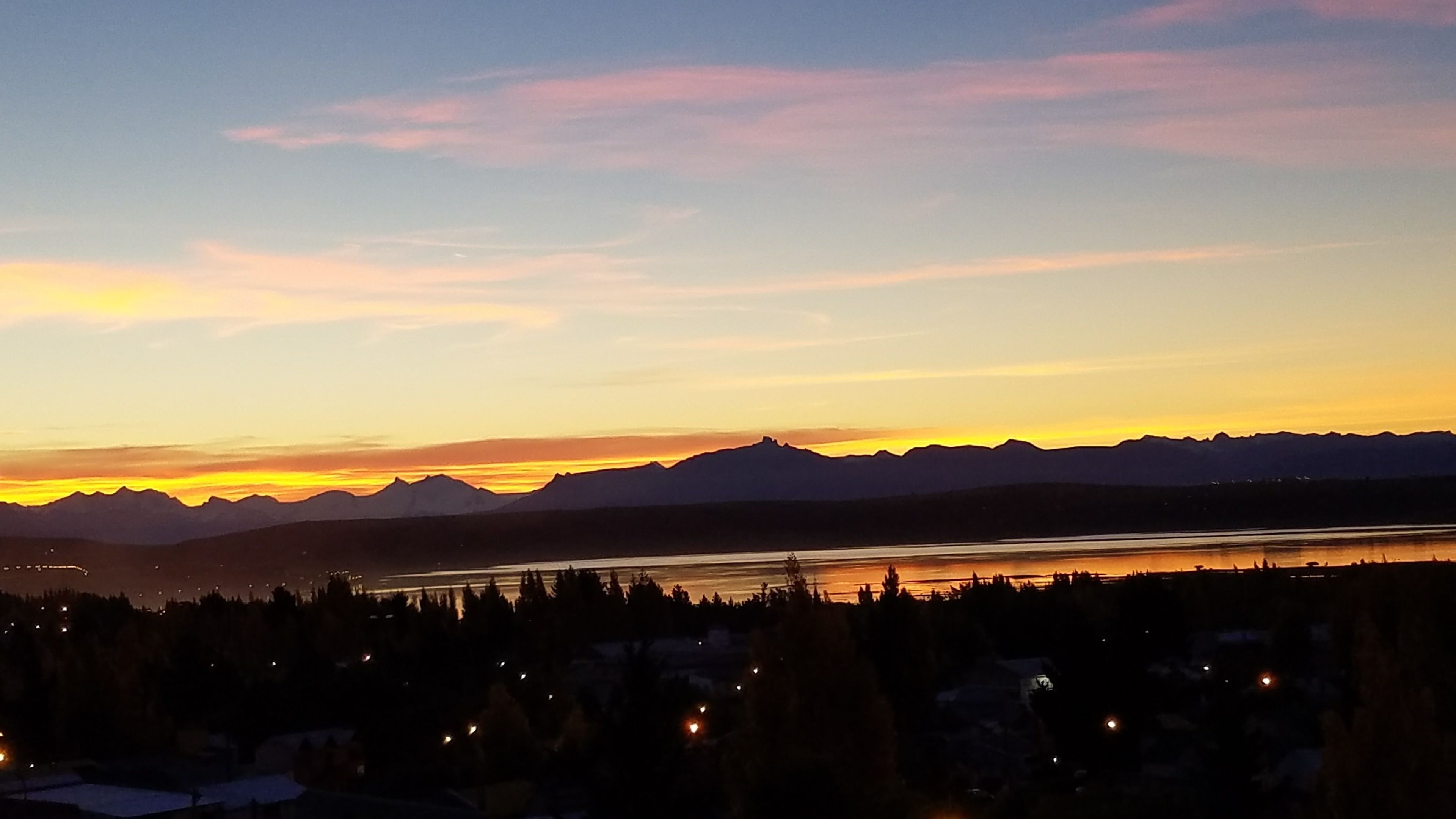 Une chaîne de montagnes au coucher du soleil, avec un lac au premier plan.