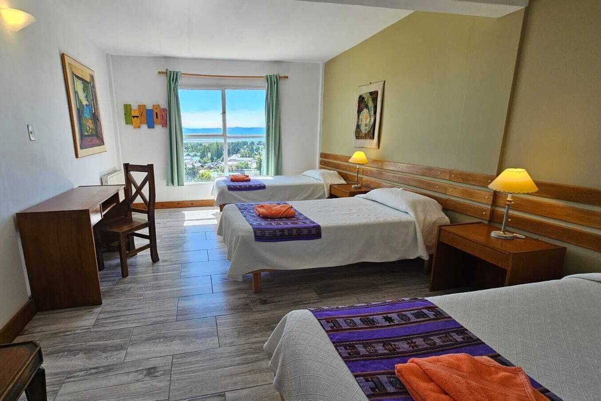Habitación de hotel con dos camas, un escritorio y una silla. Se observa una ventana con vista al paisaje.