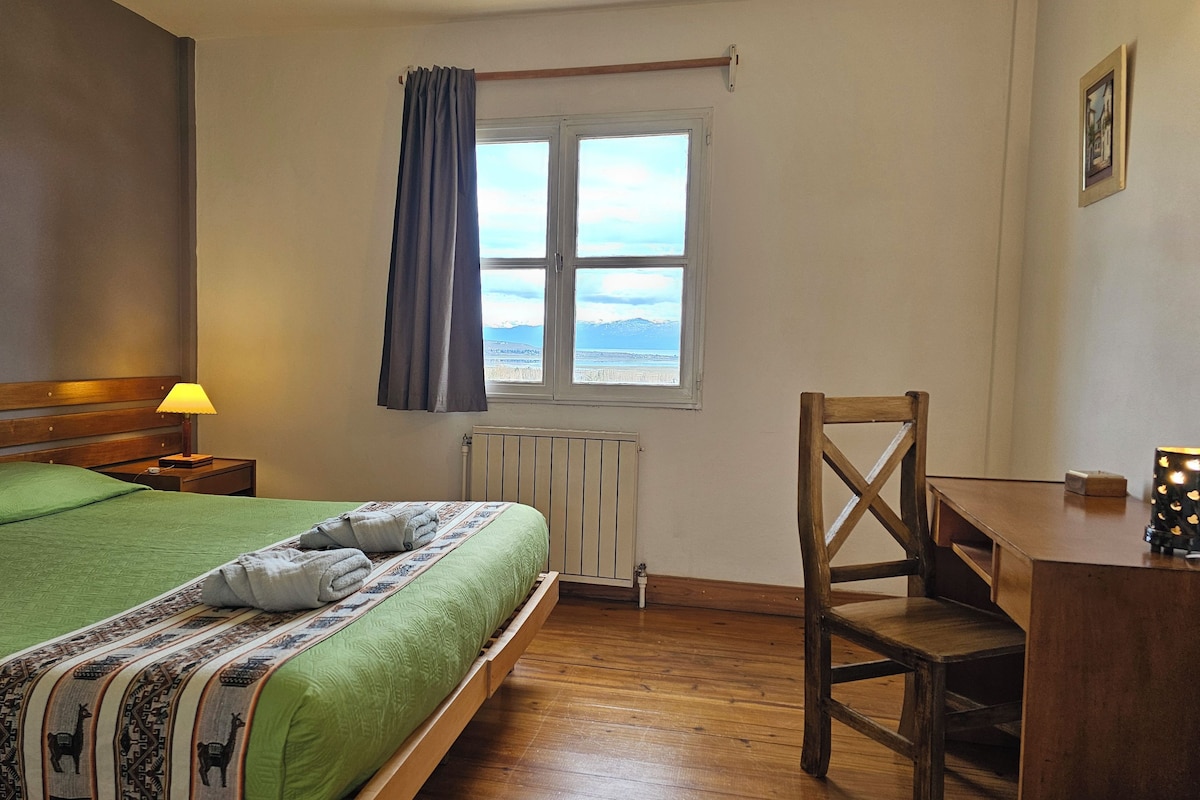Une chambre à coucher avec un lit, une chaise, une table, une fenêtre avec des rideaux et un radiateur.