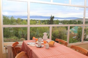 Ein Essbereich mit gedecktem Tisch für das Frühstück, Blick auf einen See und Berge, und ein Fenster mit Grünblick.