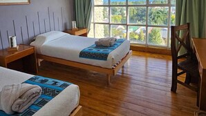 A room with two beds, a wooden floor, a large window with a view, and a painting on the wall.