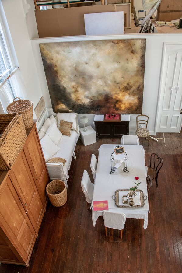 Una habitación con un cuadro abstracto grande, un aparador de madera, un sofá blanco, una mesa de comedor con una bandeja y una silla.