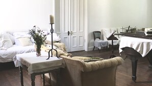 A room with a piano, a sofa, a table with a vase of flowers, and a door.