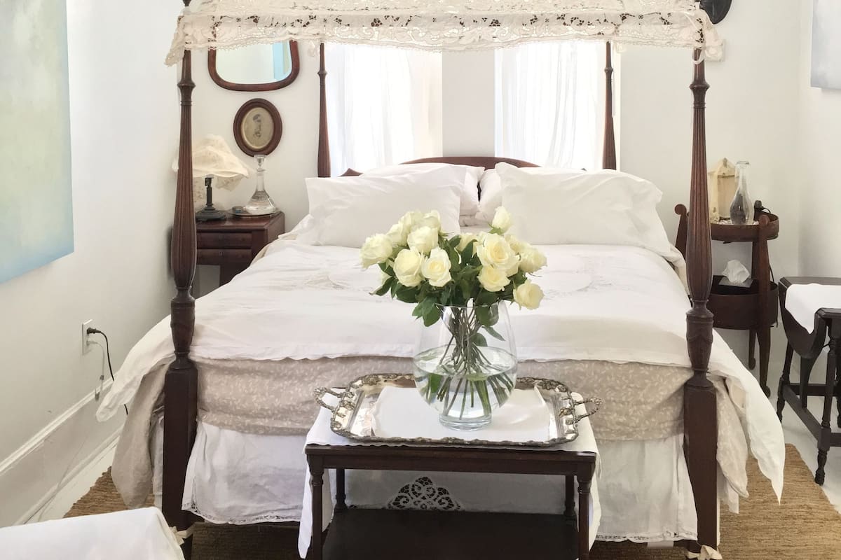 Une chambre à coucher avec un lit à baldaquin, un ventilateur de plafond, un vase de fleurs blanches et une table de chevet avec une lampe.