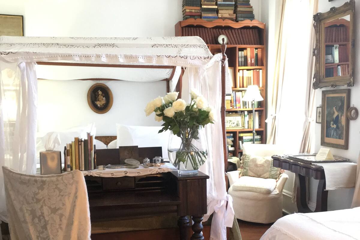 Une chambre à coucher avec un lit à baldaquin, un bureau en bois, une chaise, une bibliothèque et une table de chevet.