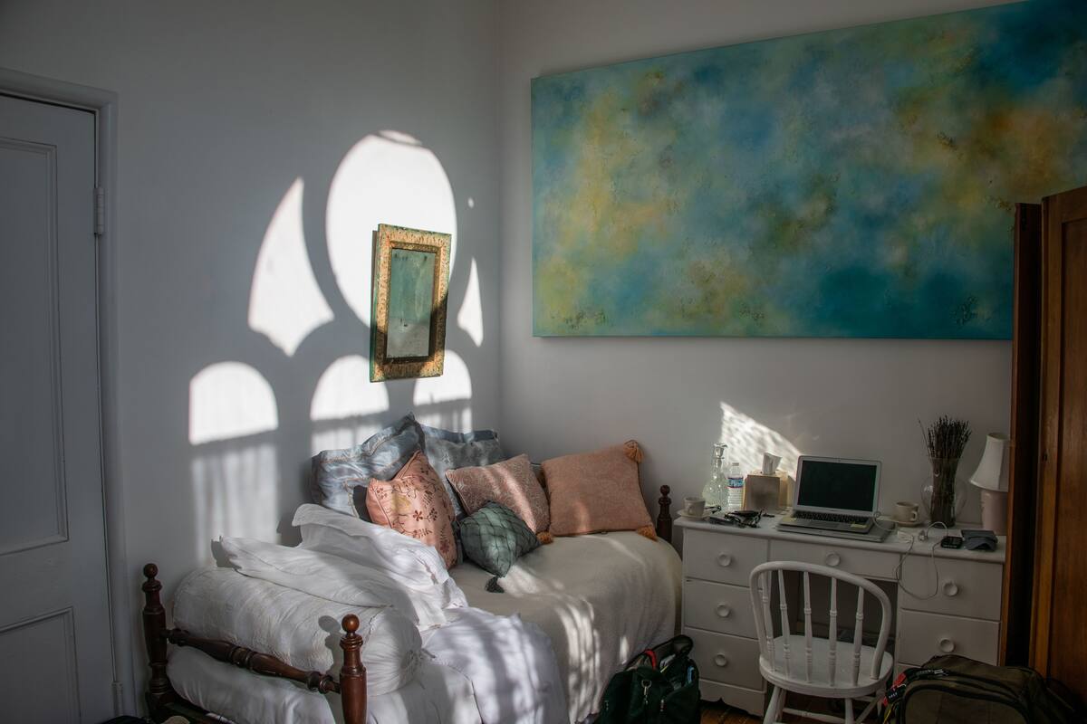 Une chambre à coucher avec un lit, un bureau avec un ordinateur portable, une chaise et un grand tableau abstrait accroché au mur.