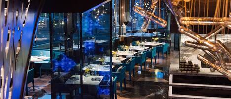 A modern restaurant with glass partitions, blue chairs, and a decorative metal sculpture.