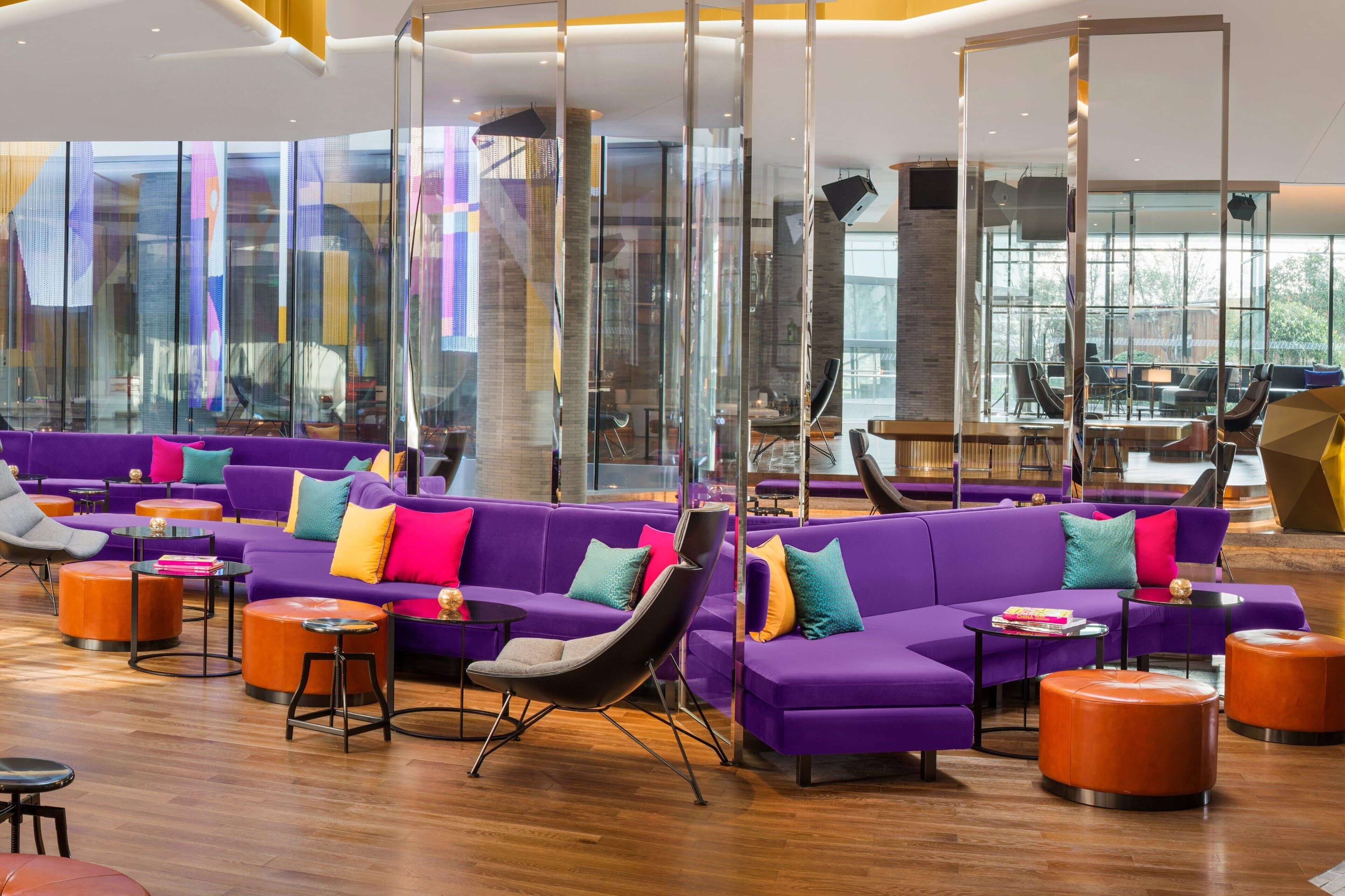 A modern lounge area with purple sofas, orange ottomans, and black chairs.