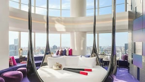 A modern room with a unique spherical bed design, large windows offering a city view, and purple accents.