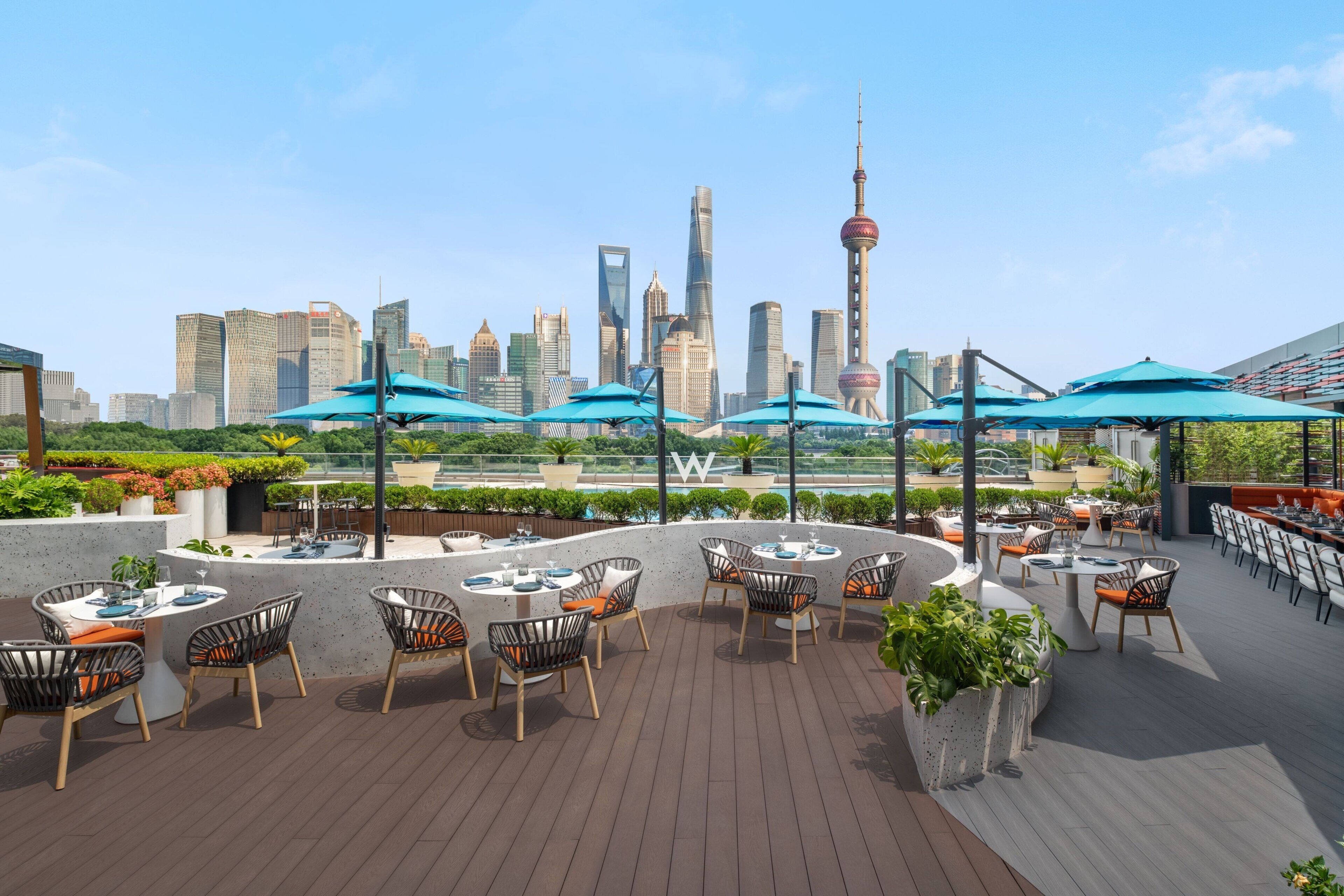 A rooftop terrace with tables and chairs, a view of the city skyline, and a large tower.
