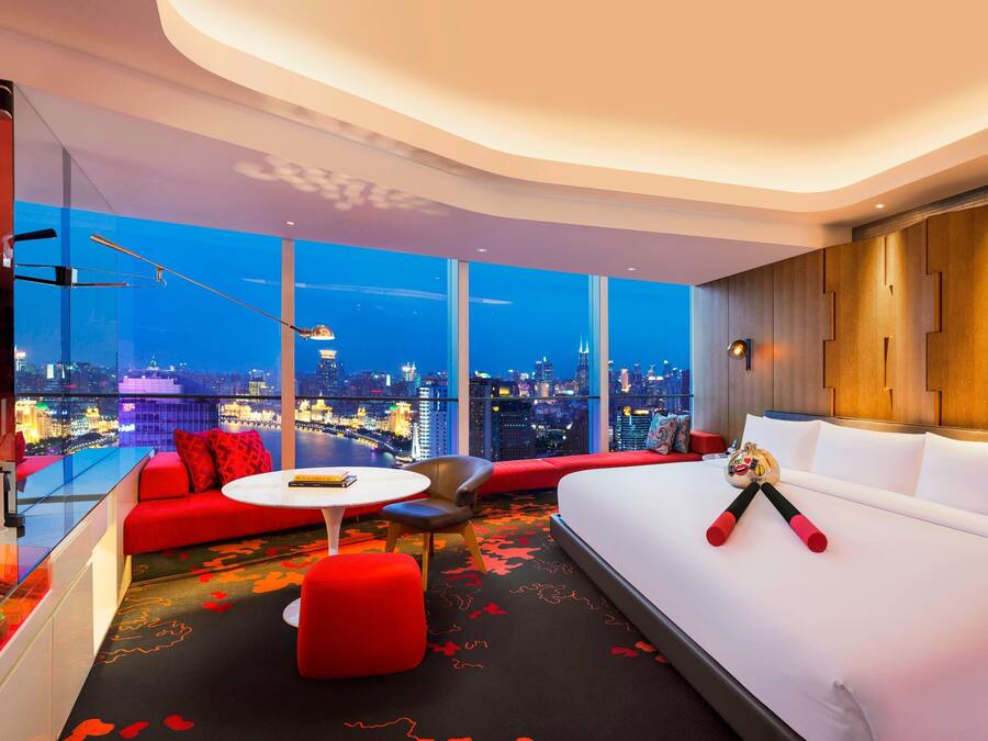 Habitación de hotel moderna con amplia vista a la ciudad, un sofá, una cama y una pequeña mesa.