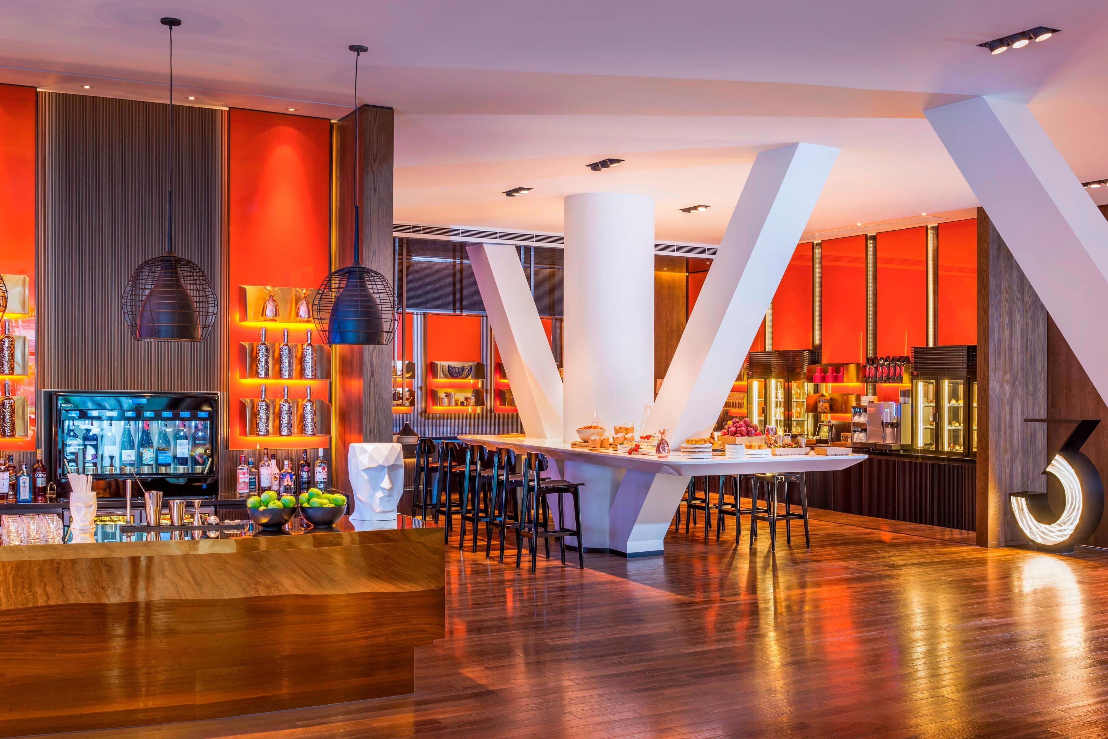 A modern bar area with a wooden bar counter, multiple seating options, and a large television screen.