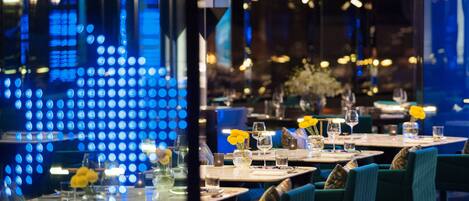 A restaurant with tables set for dining, featuring blue ambient lighting and yellow flowers on the tables.