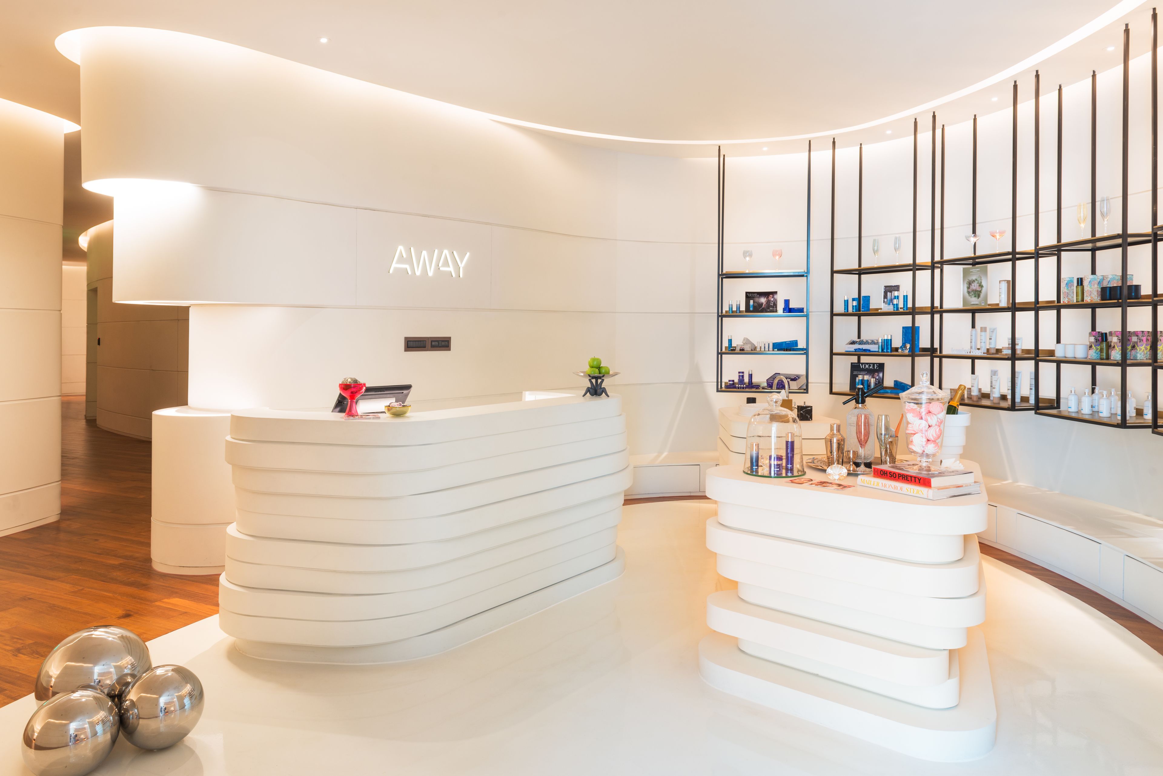 Un área de recepción moderna con un mostrador blanco curvo, una estantería con diversos objetos y un diseño limpio y minimalista.