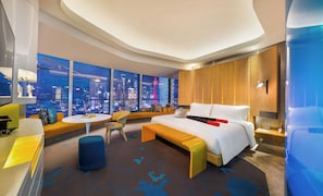 Una habitación de hotel moderna con vista a la ciudad, una cama grande, un sofá, una mesita y un escritorio.