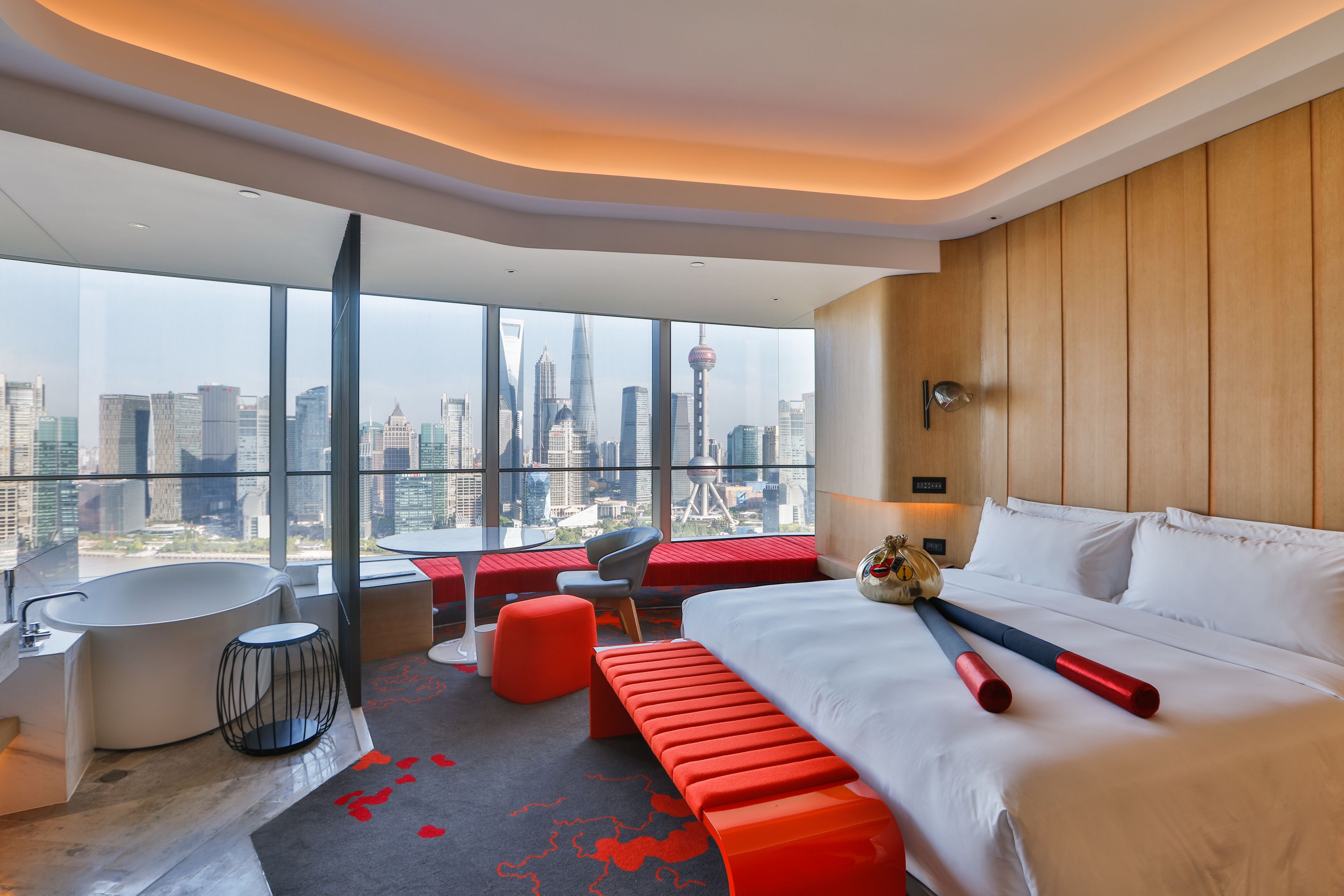 A modern hotel room with a large bed, a sitting area, a bathtub, and a city view.
