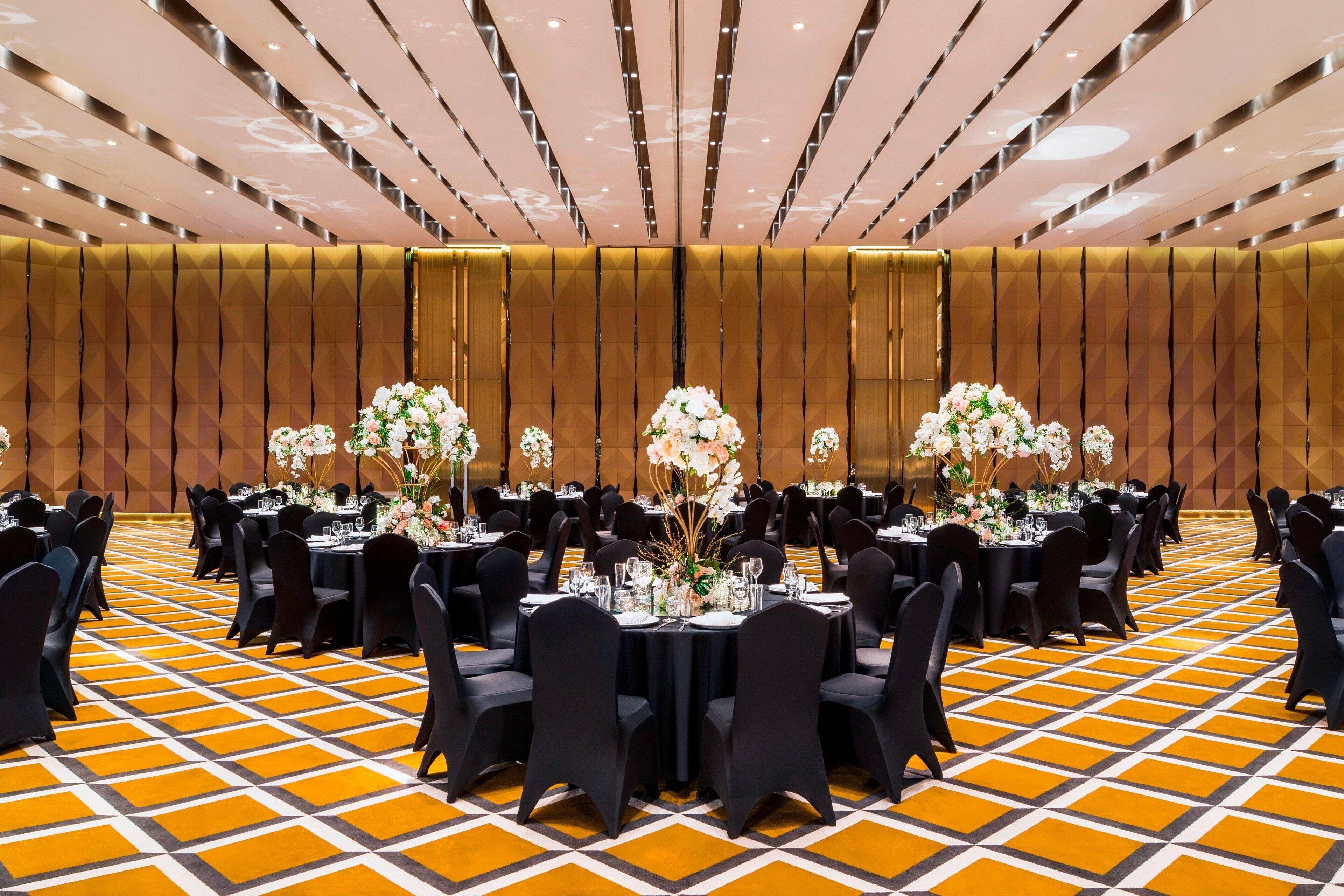 Une salle de banquet avec des tables rondes, des chaises noires et des centres de table floraux.
