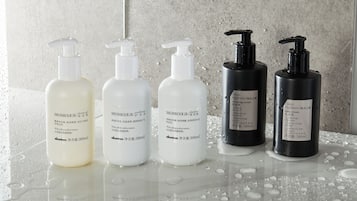 Four bottles of MOMO bath products on a reflective surface with water droplets, against a textured wall.