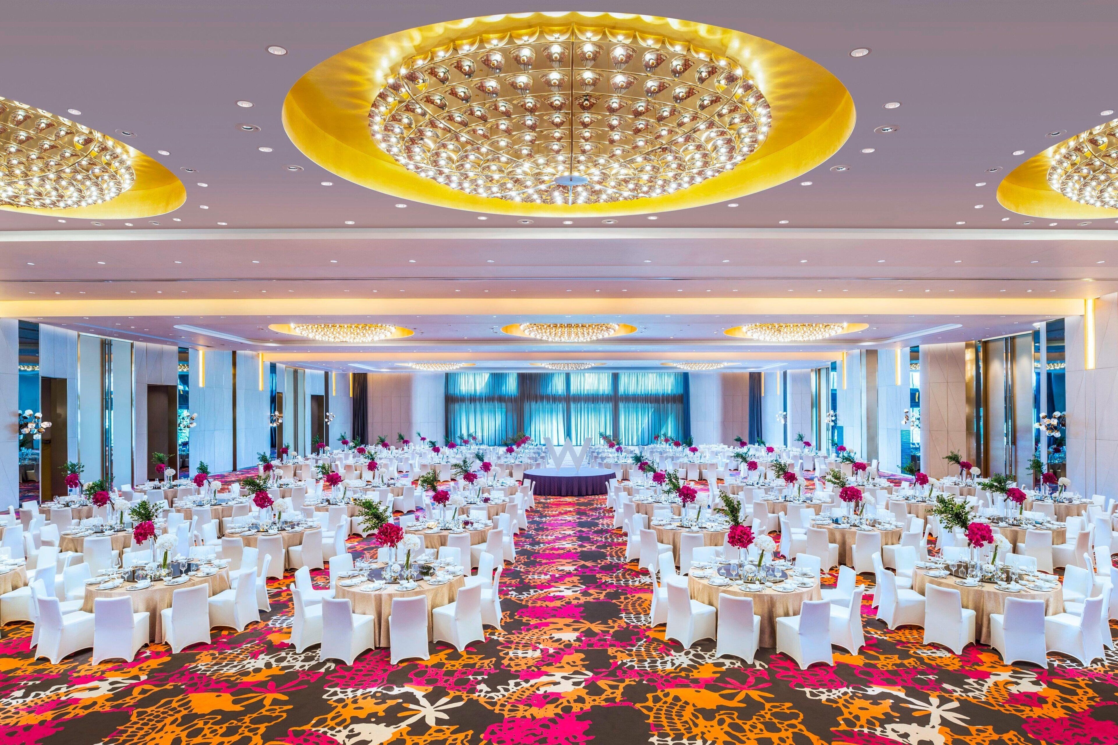 A banquet hall with round tables, white chairs, and a central aisle.