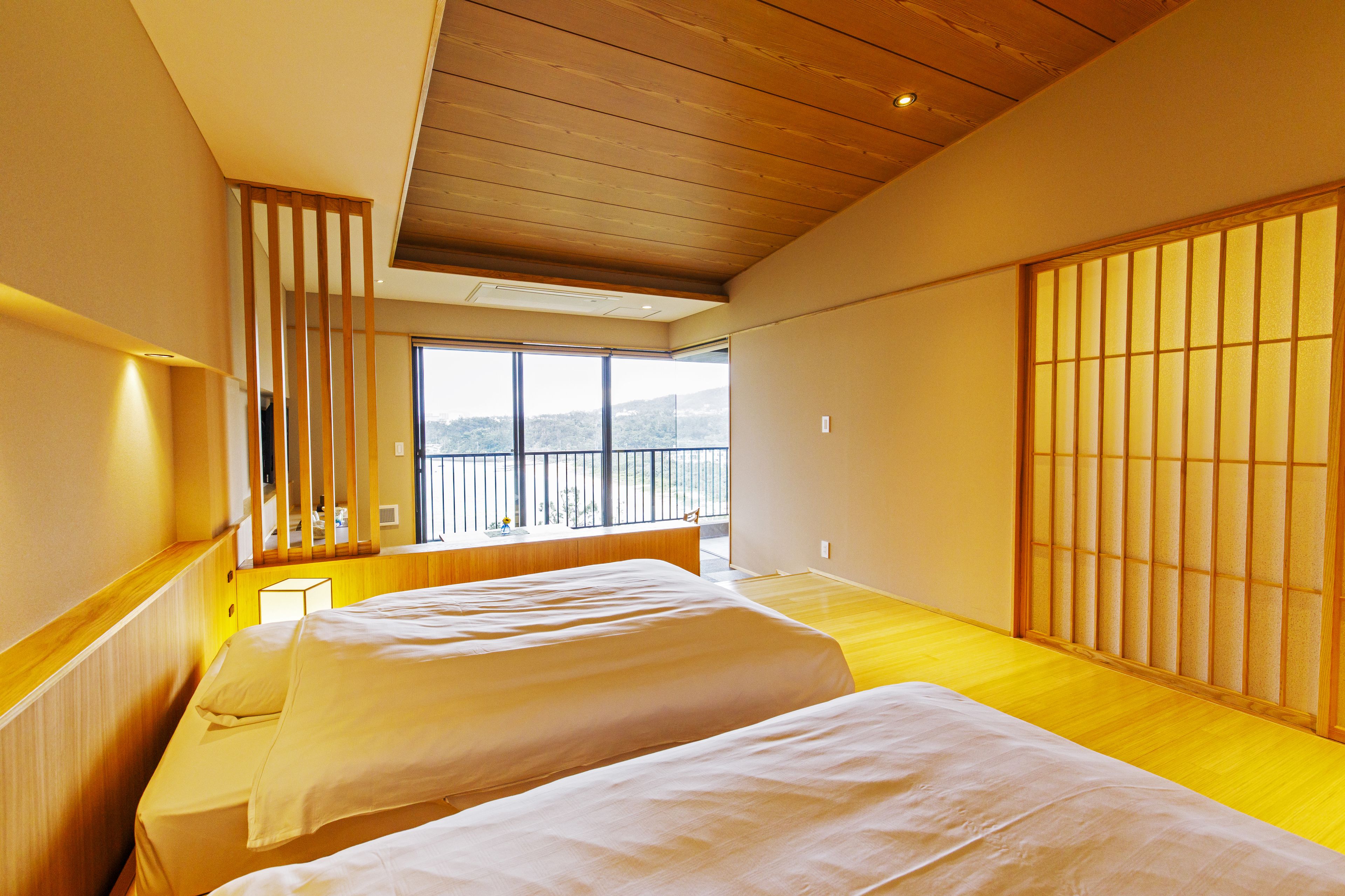 Habitación de hotel con dos camas, suelo de madera, balcón con vistas y puertas correderas tradicionales japonesas.
