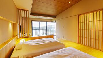 Habitación de hotel con dos camas, suelo de madera, balcón con vistas y puertas correderas tradicionales japonesas.