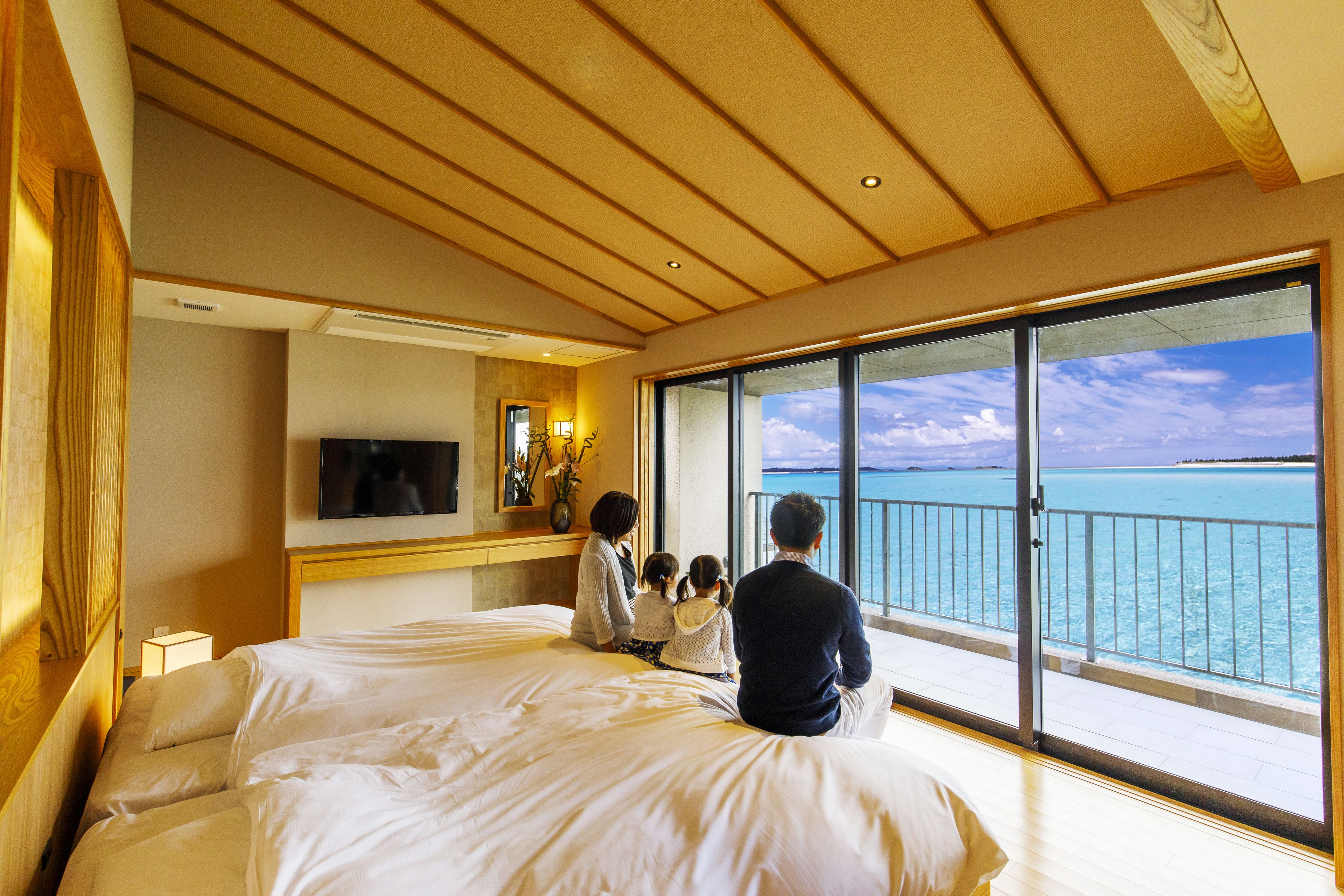 A hotel room with a large bed, a TV, a desk, and a balcony with a view of the ocean.