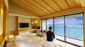 A hotel room with a large bed, a TV, a desk, and a balcony with a view of the ocean.