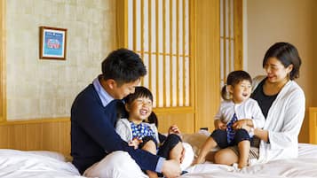 A family of four on a bed in a room with a wooden headboard and a framed picture on the wall.